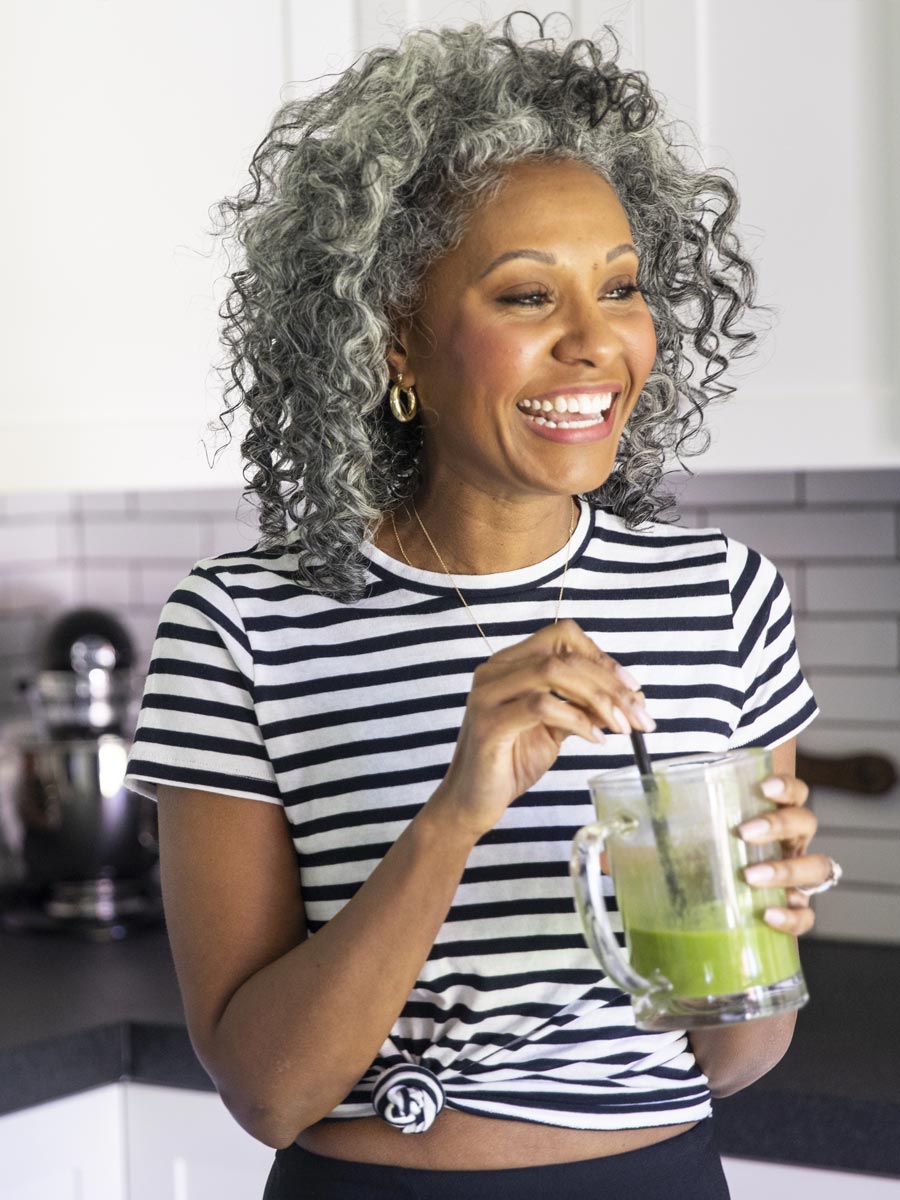 Lachende Frau, die grünen Smoothie in der Küche trinkt